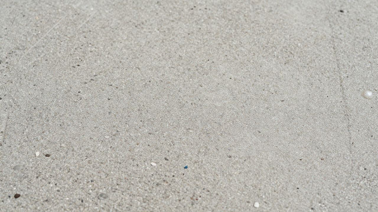 Close-up of a textured non-slip painted concrete surface outdoors with visible fine aggregate grain and a few water droplets sitting on top